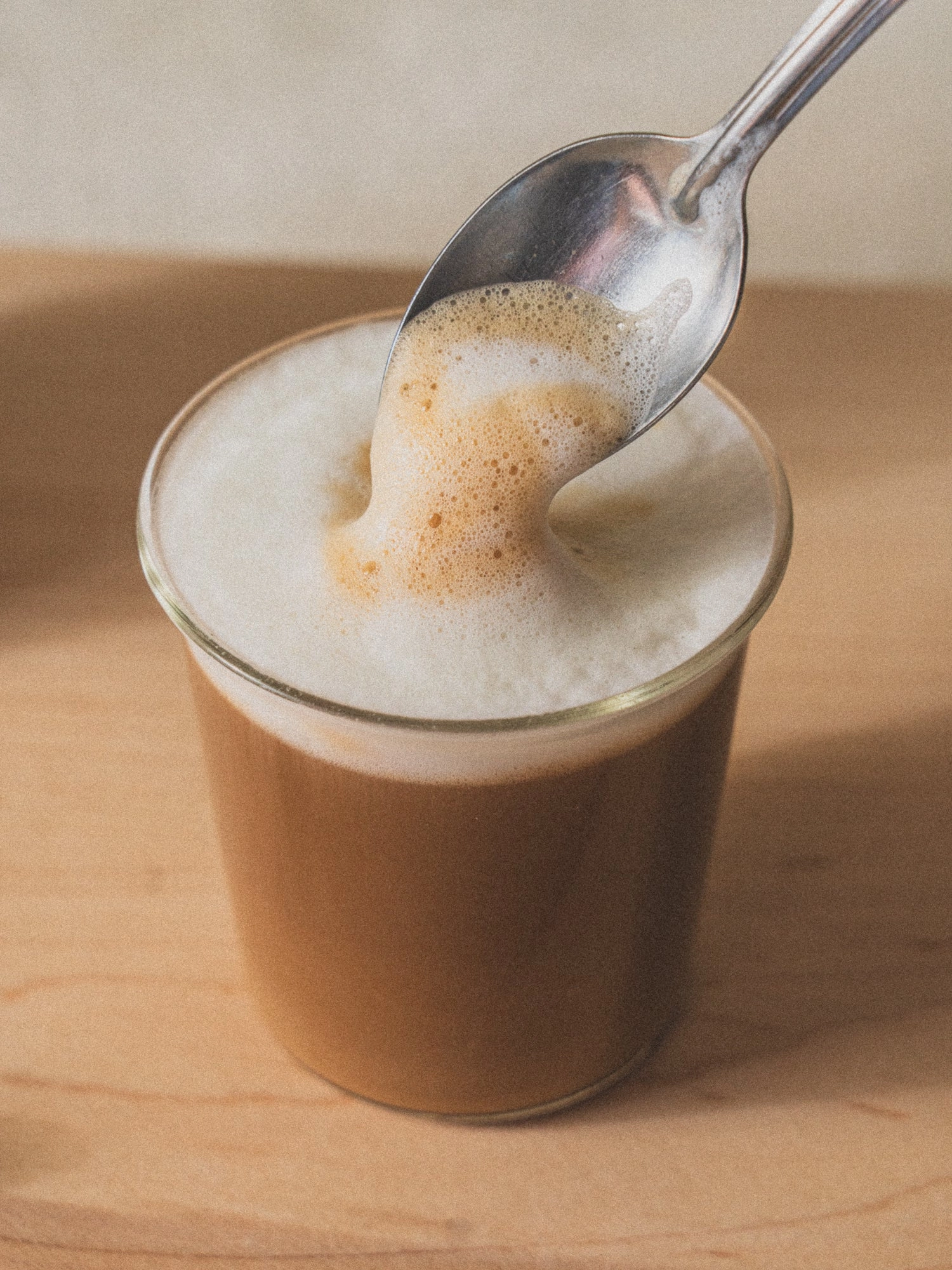 A spoon lifting foam from a latte in a glass