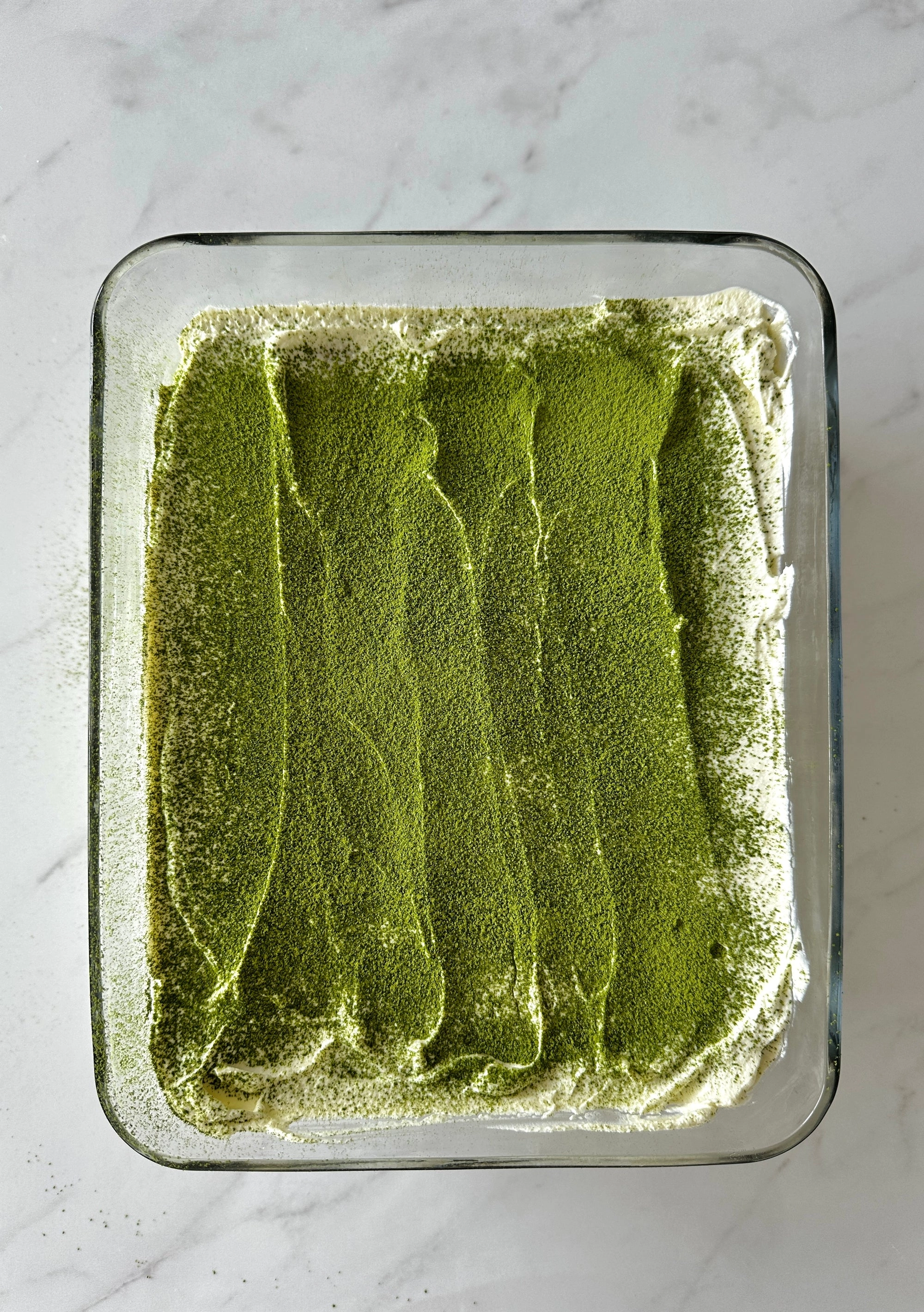 Matcha Tiramisu in a glass dish, dusted with green powder
