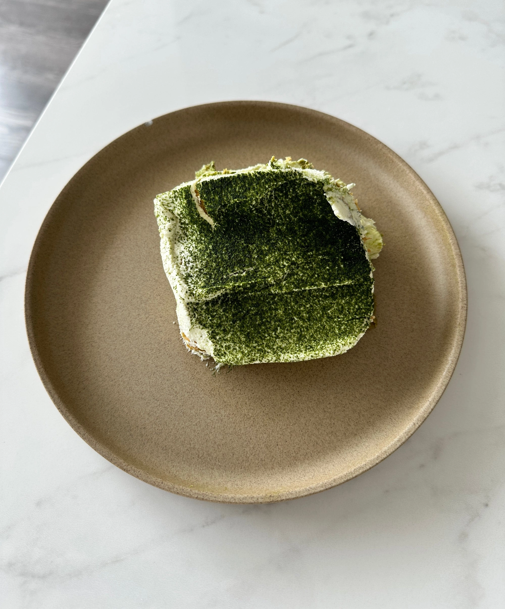 A slice of matcha tiramisu on a stoneware plate, set on a marble table