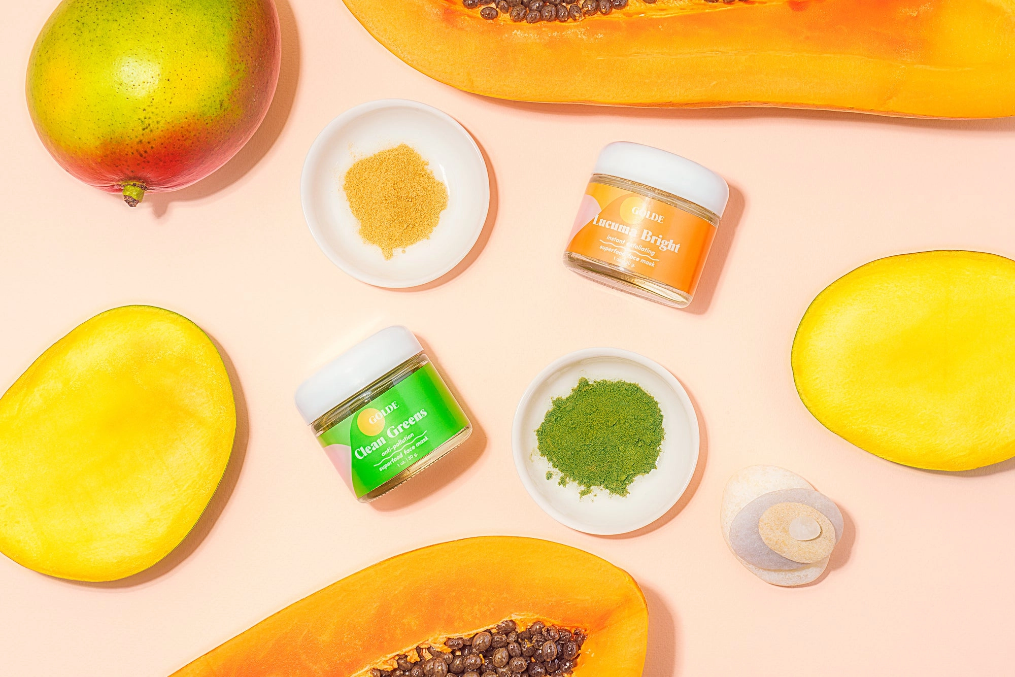 Papaya, mango and small jars of superfood face mask powders on a pink surface