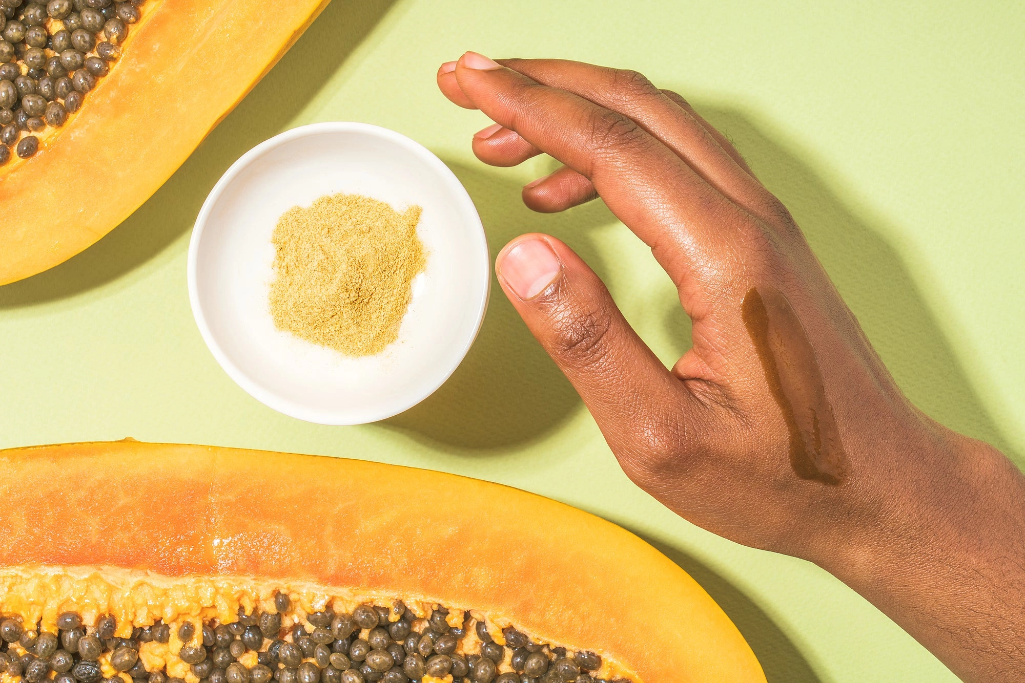 A hand reaching for a dish of mask powder between papaya halves